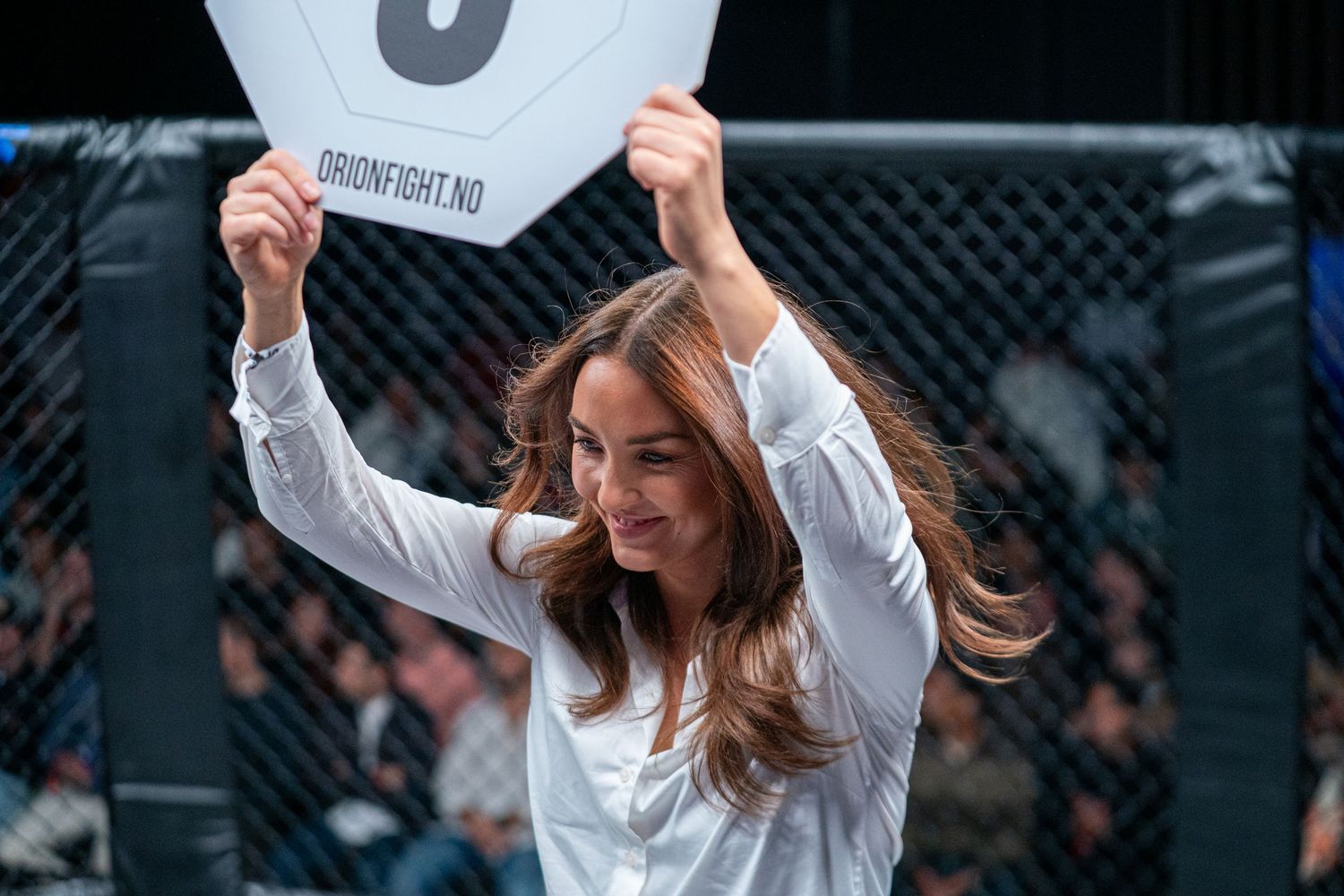A person in a white top celebrates joyfully with raised arms in front of a dark background.