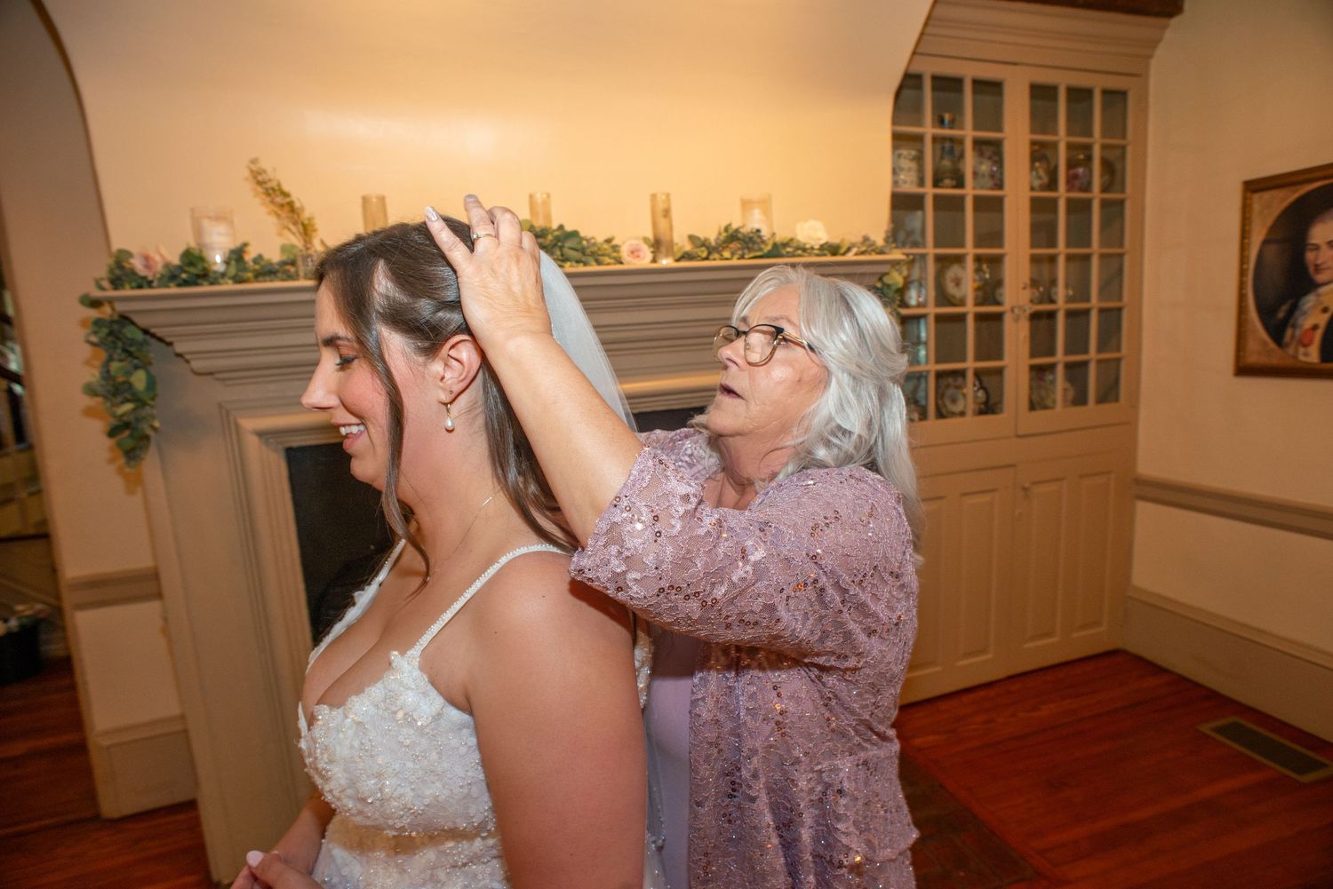 A tender moment captured during wedding preparations in a warmly lit room with hardwood floors and traditional decor.