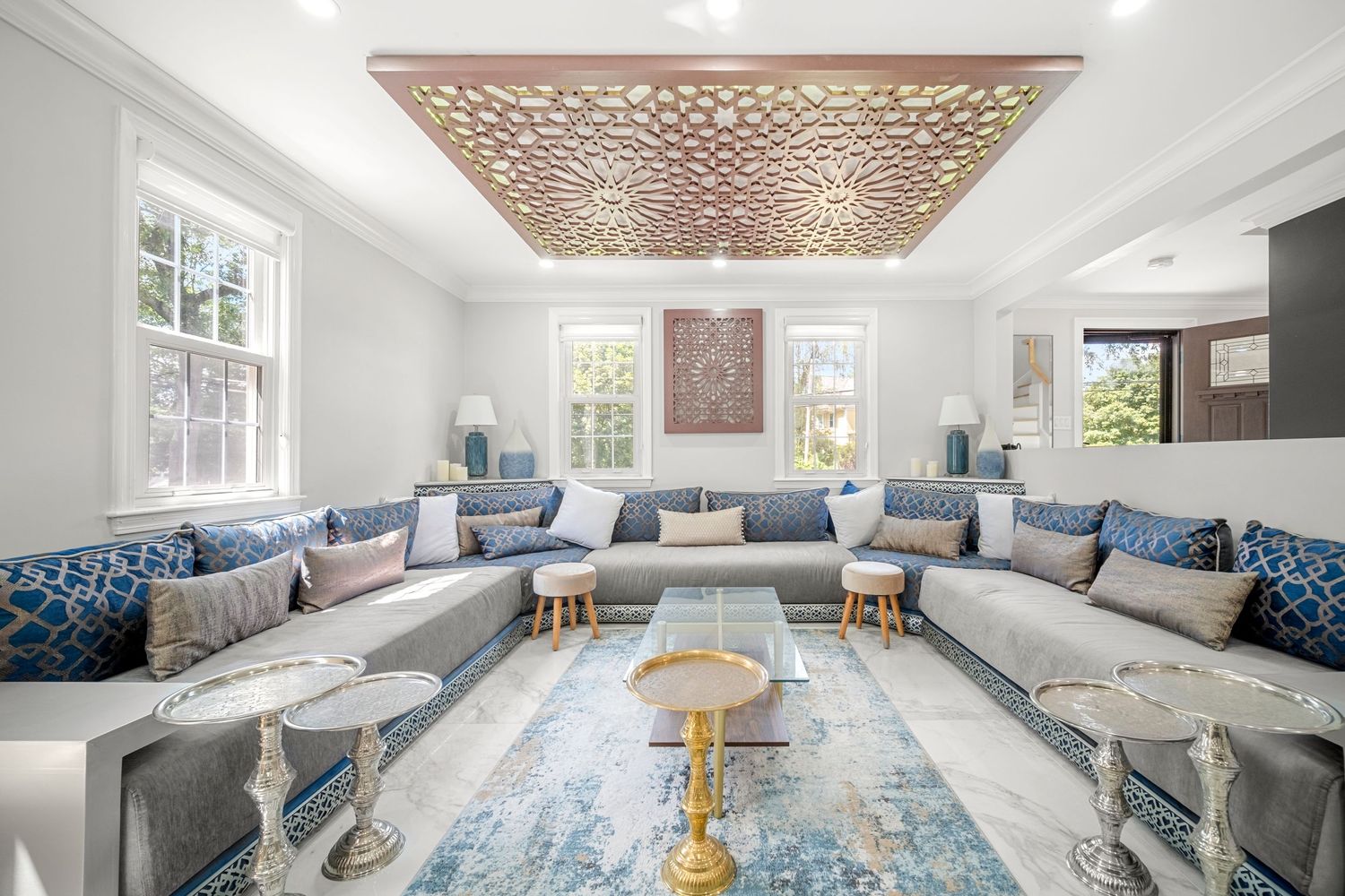 Luxurious Moroccan-inspired living room with ornate ceiling panel, blue sectional sofas, and gold accents.