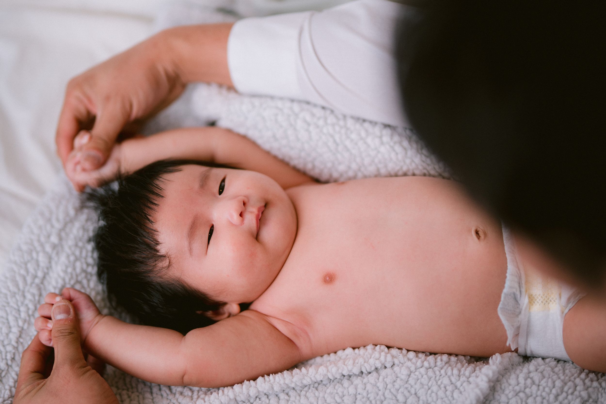 A peaceful baby rests on white textured blanket during a tender moment.