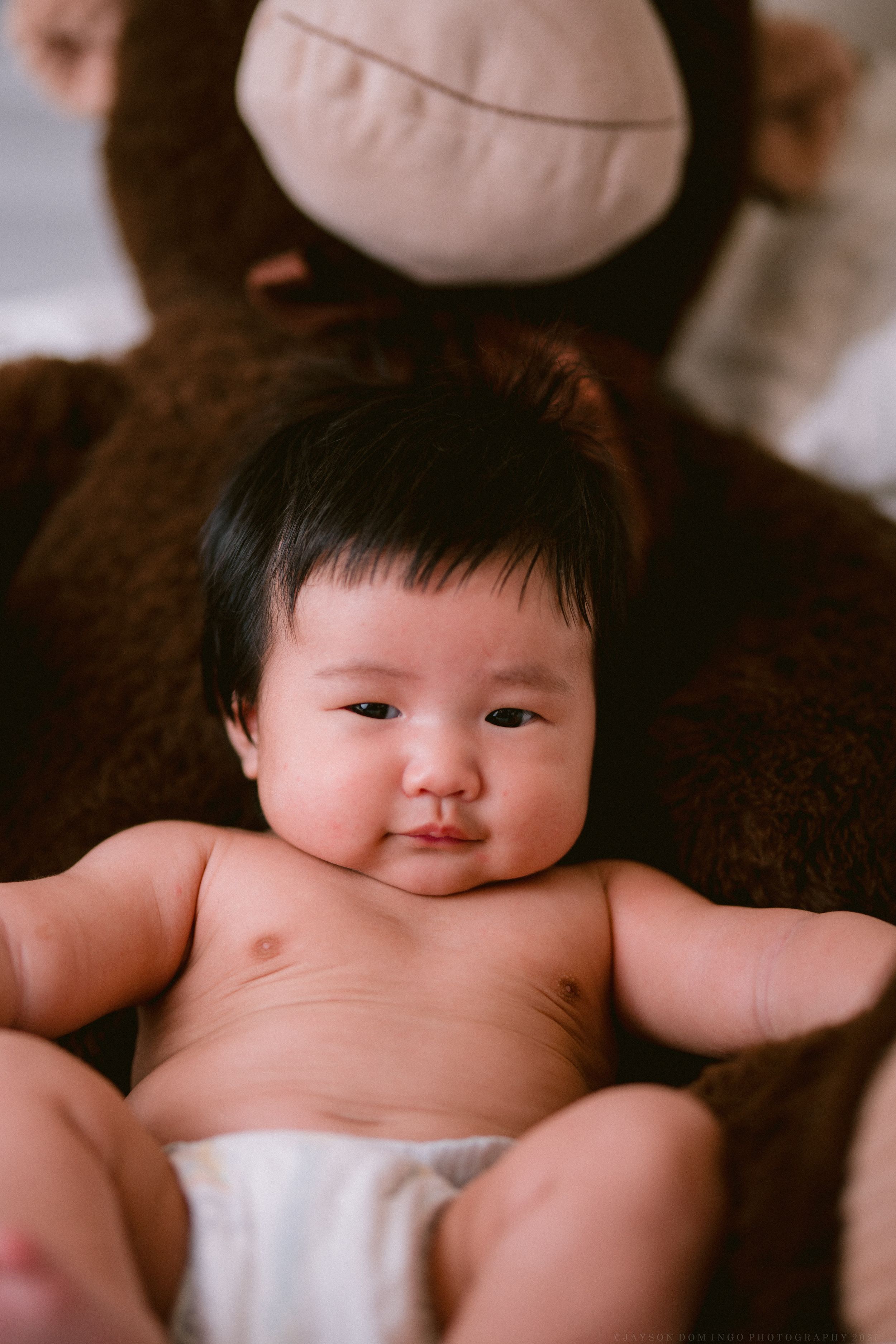 Adorable baby lying on soft brown blanket showing chubby cheeks and bare tummy.