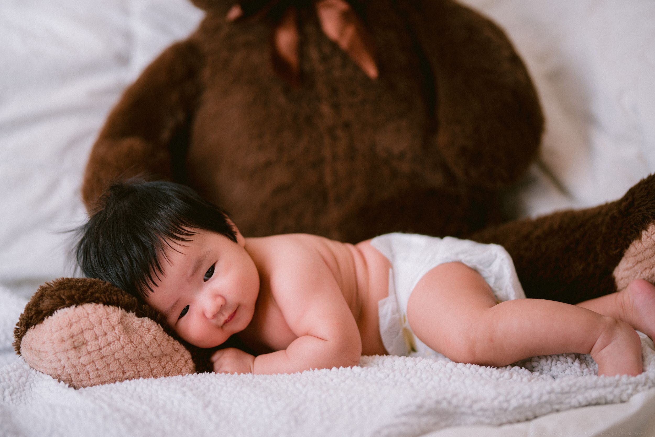 Baby sleeping peacefully next to soft brown plush toy on white textured surface.