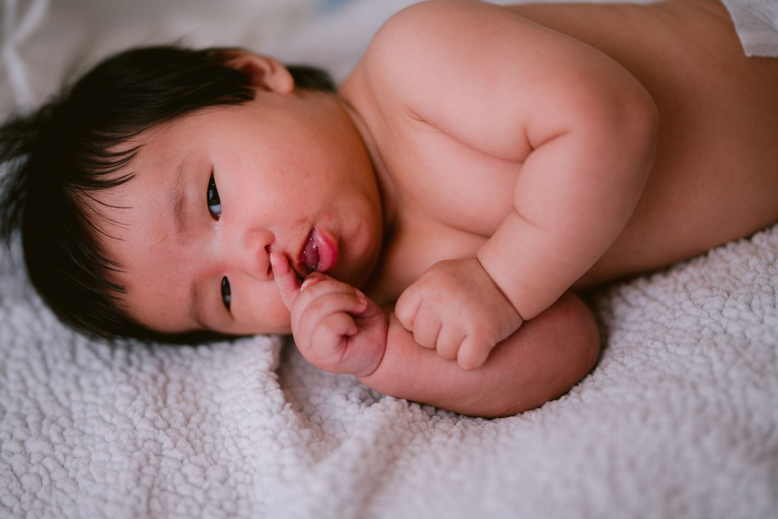 Sweet infant resting peacefully on white textured blanket with dark hair.