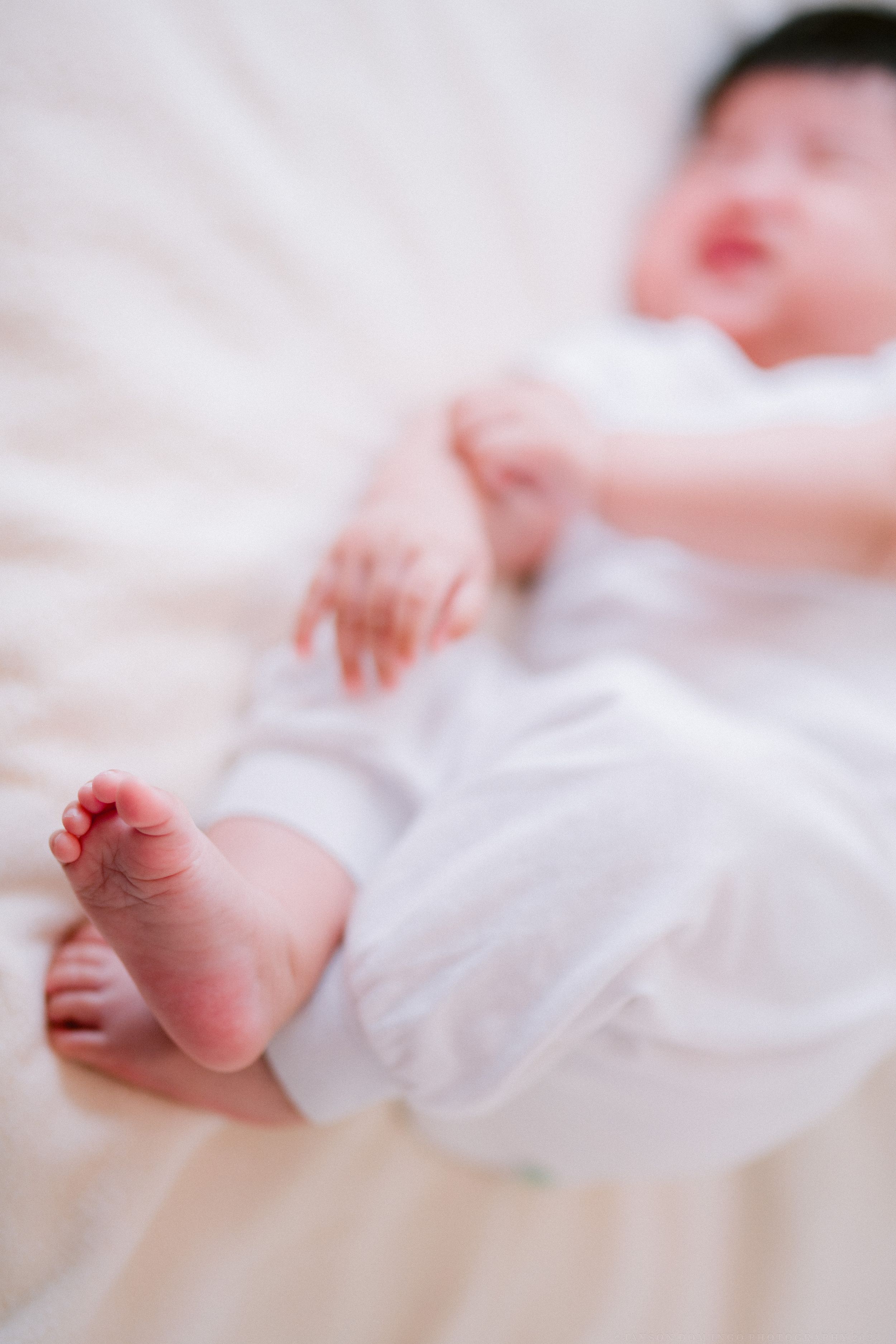 Close-up view of tiny newborn baby feet wrapped in soft white fabric against a light background.