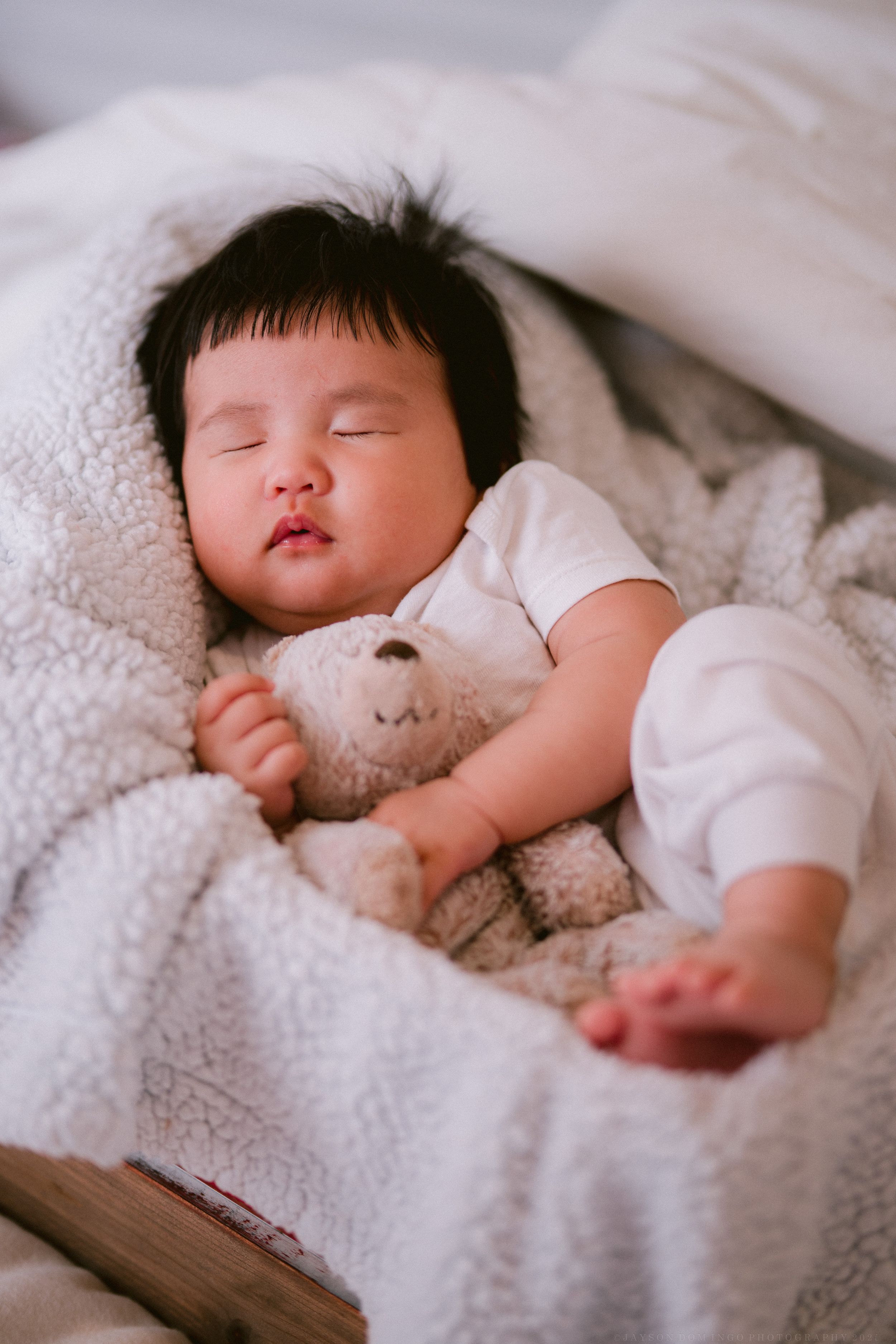 Baby in white onesie sleeping soundly on fluffy white blanket in sequential photos.