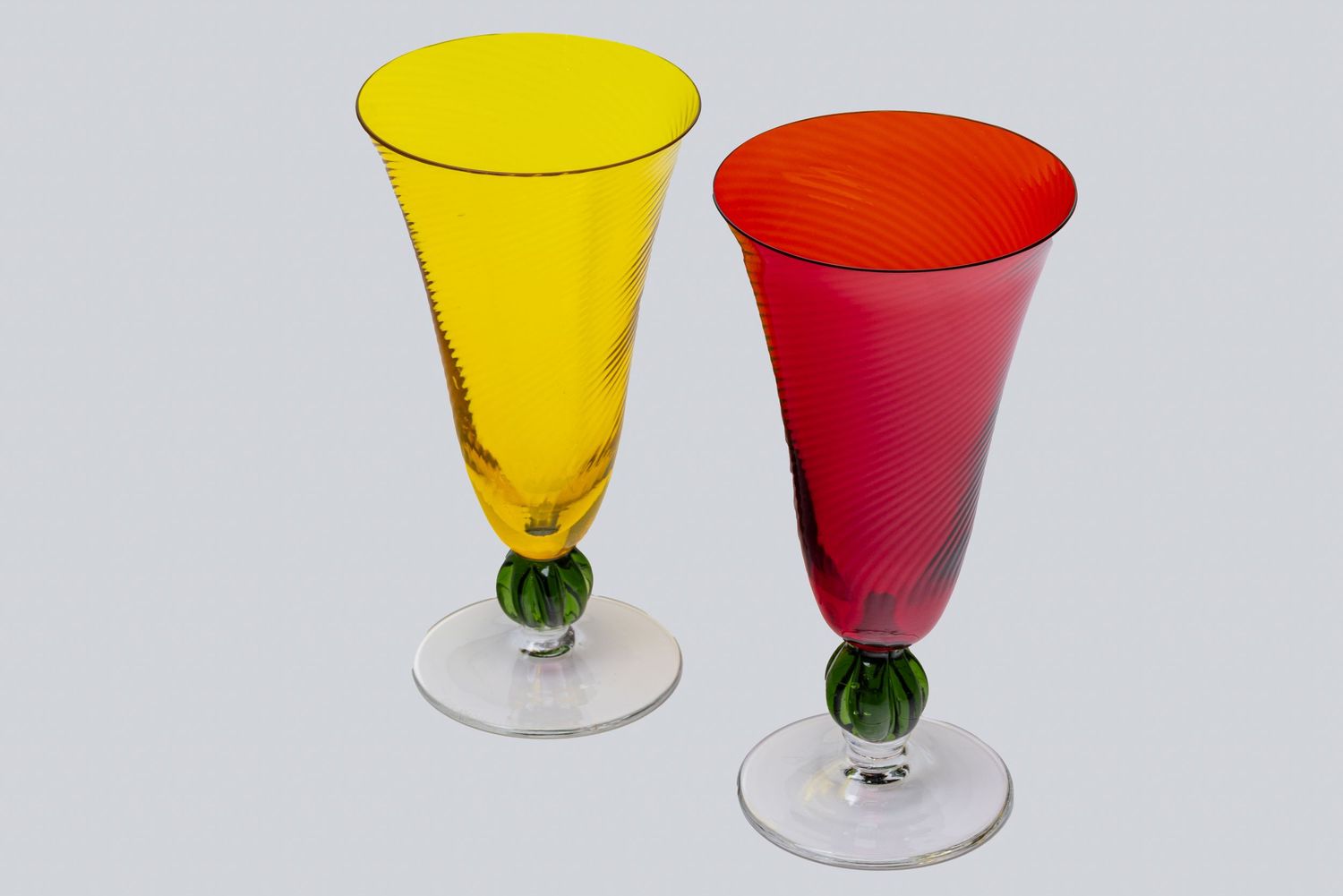 Two elegant glass goblets with green bubble stems, one in bright yellow and one in vibrant red, displayed side by side.