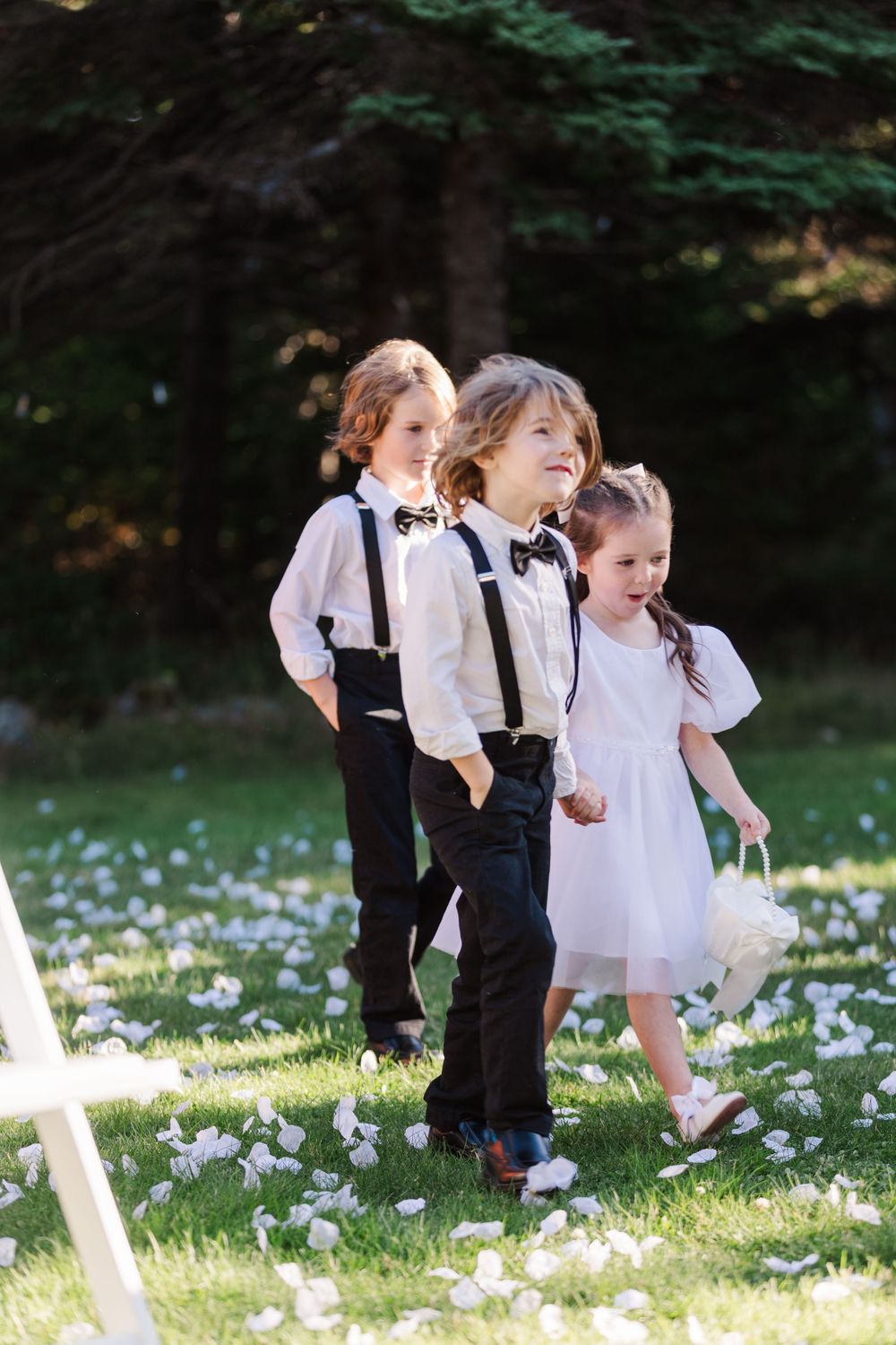 Children in formal black and white attire playing together in a grassy field with scattered white flowers.
