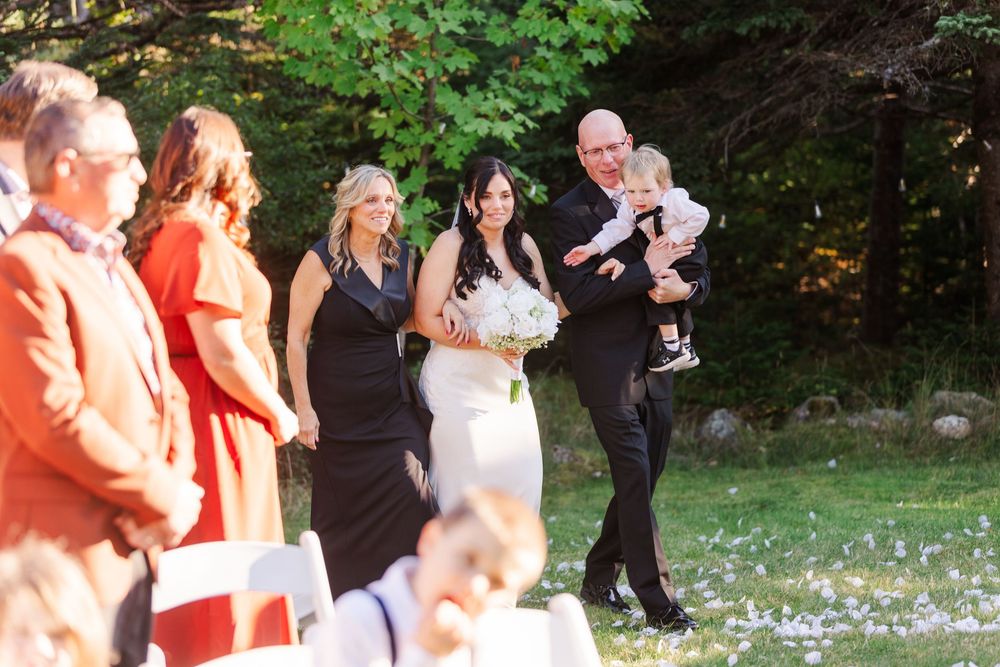 Wedding guests toss white flower petals in celebration at an outdoor garden ceremony.