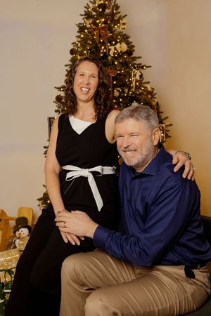 A couple shares a joyful moment together in front of a decorated Christmas tree.