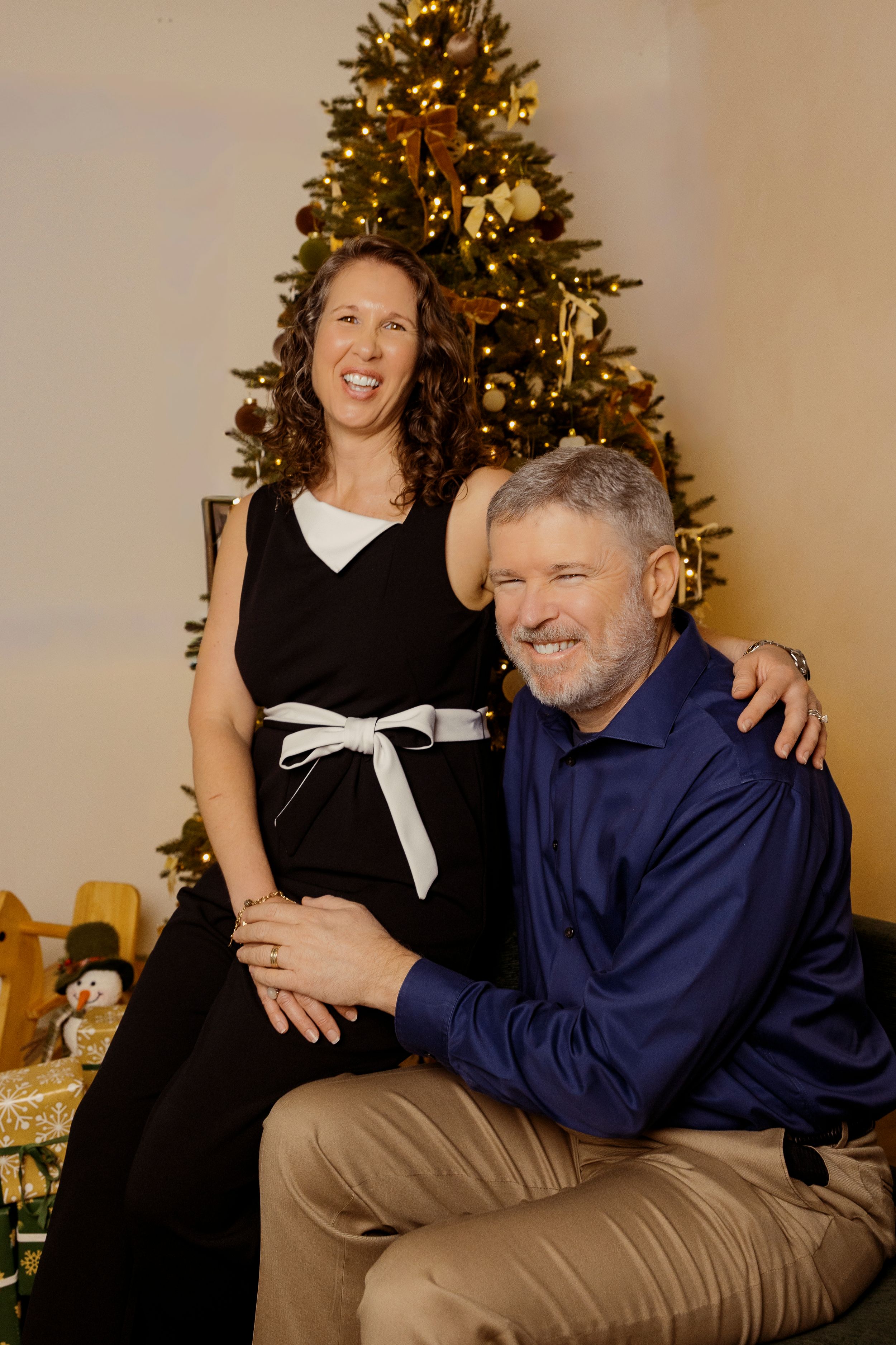A couple shares a joyful moment together in front of a decorated Christmas tree.