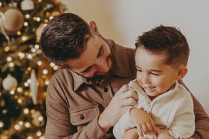Parent and child share tender moments during Christmas while sitting near decorated tree with warm lighting.