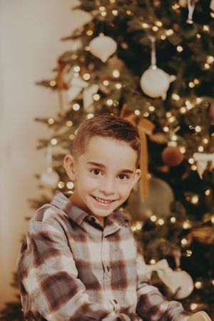 Festive holiday portrait in front of decorated Christmas tree with warm lighting and ornaments.