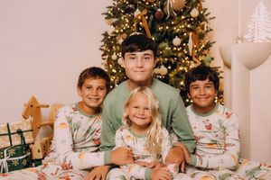 A group in matching Christmas pajamas sits together in front of a decorated tree with presents underneath.