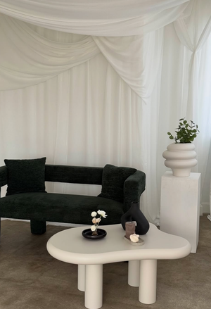 Modern white lounge area with black sofa and cylindrical pedestal tables creating a minimalist aesthetic.
