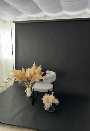 White chaise lounge with pampas grass decor in a dark studio setting creates an elegant minimalist atmosphere.