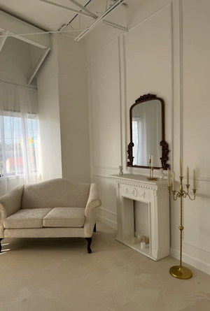Elegant white studio space with wainscoting, natural light, and a cream chaise lounge against paneled walls.