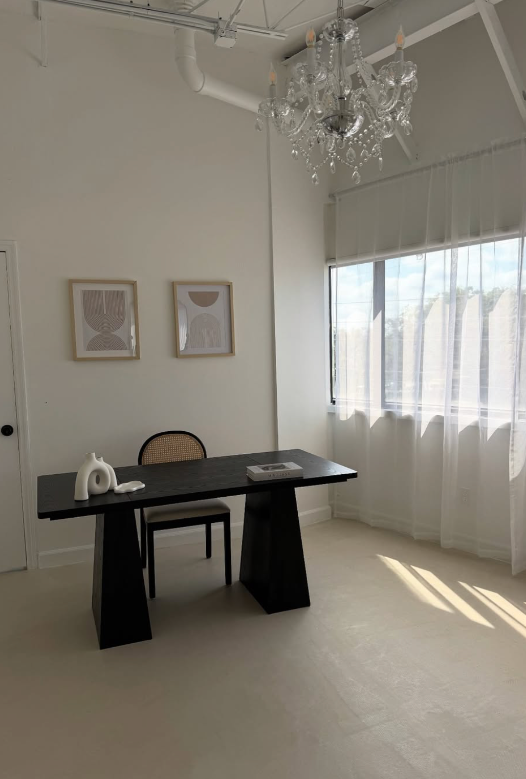 Bright white photography studio space with crystal chandeliers, black desk, and natural light streaming through windows.