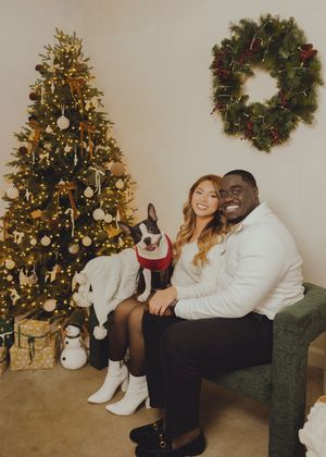 A couple poses together for Christmas photos near a decorated tree and holiday wreath in a cozy home setting.