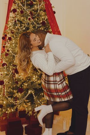 A romantic holiday moment captured in front of a lit Christmas tree with red decorations.