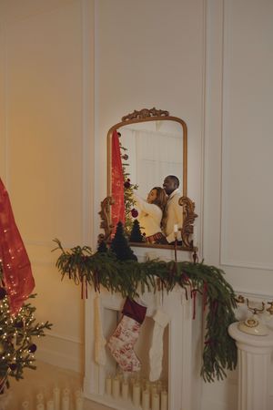 Elegant Christmas mantel decorated with red ribbons, greenery and ornate holiday decorations along a white fireplace.
