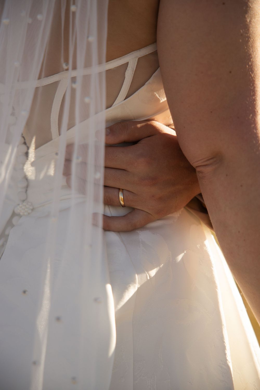 Close-up detail shots of a white wedding dress with delicate lace and button details in soft natural light.
