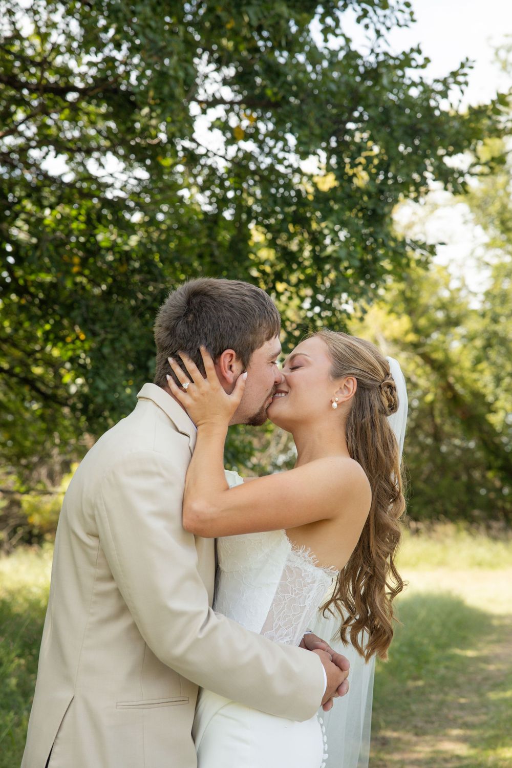 A romantic outdoor wedding moment captured in a garden setting with sunlight filtering through the trees.