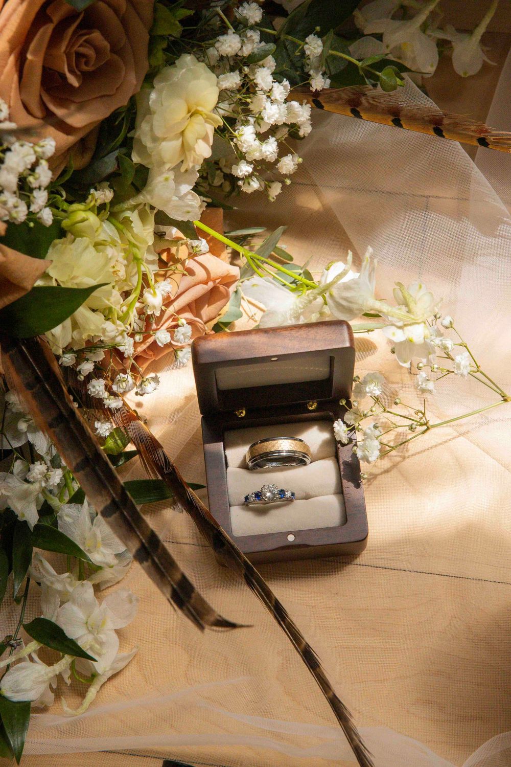 A series of elegant wedding rings in jewelry boxes surrounded by delicate white flowers and roses on a light surface.