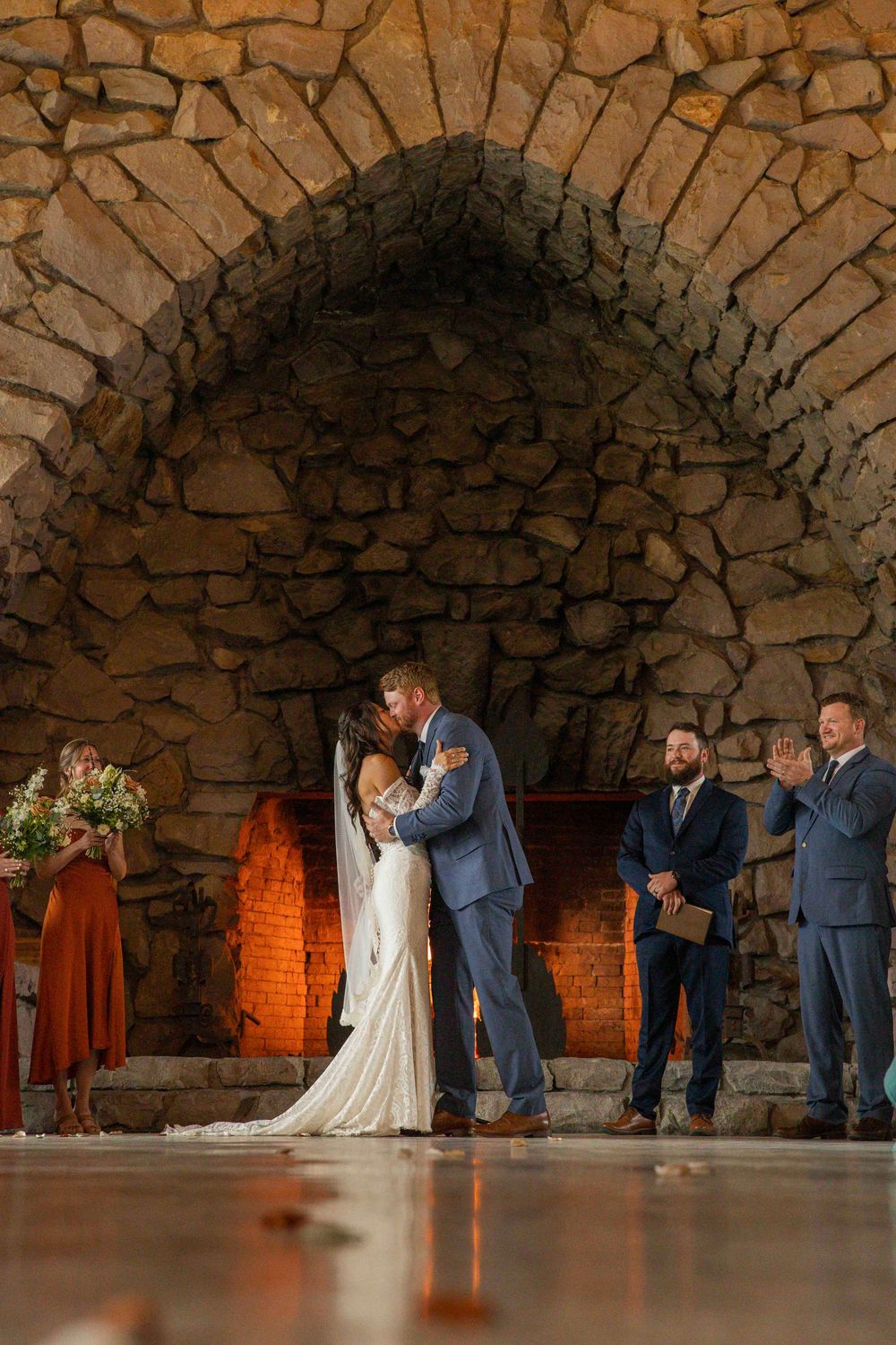 Wedding party stands under a rustic stone archway with warm lighting during an intimate ceremony.