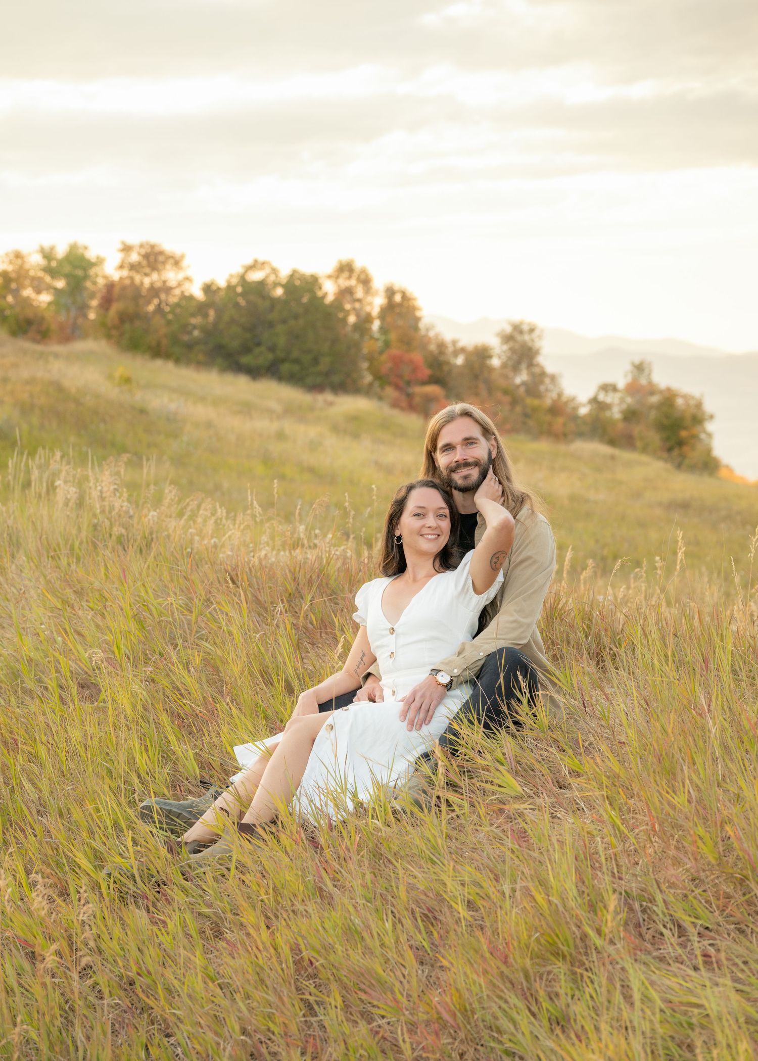 Couple lounges together in a golden autumn meadow at sunset wearing white outfits.