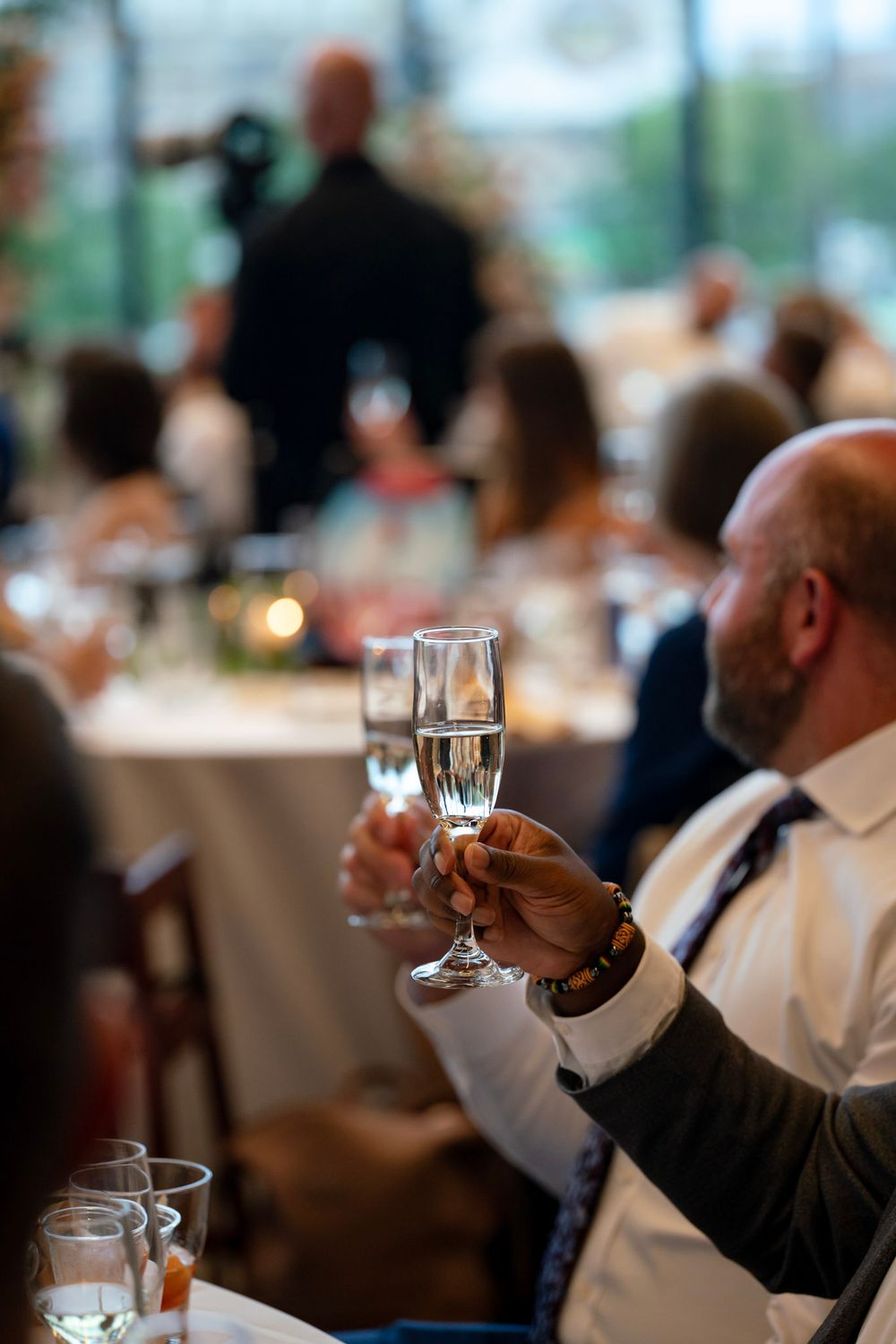 Guests hold up wine glasses in a toast during an elegant dinner event with soft lighting and blurred background.