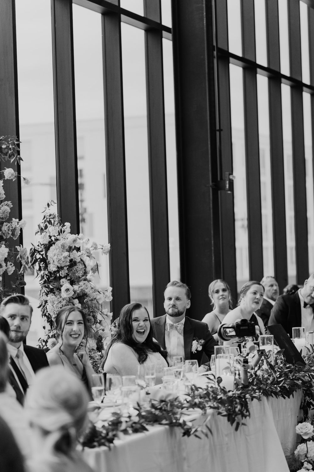 Long banquet table decorated with floral arrangements and candles at an elegant reception with guests seated.