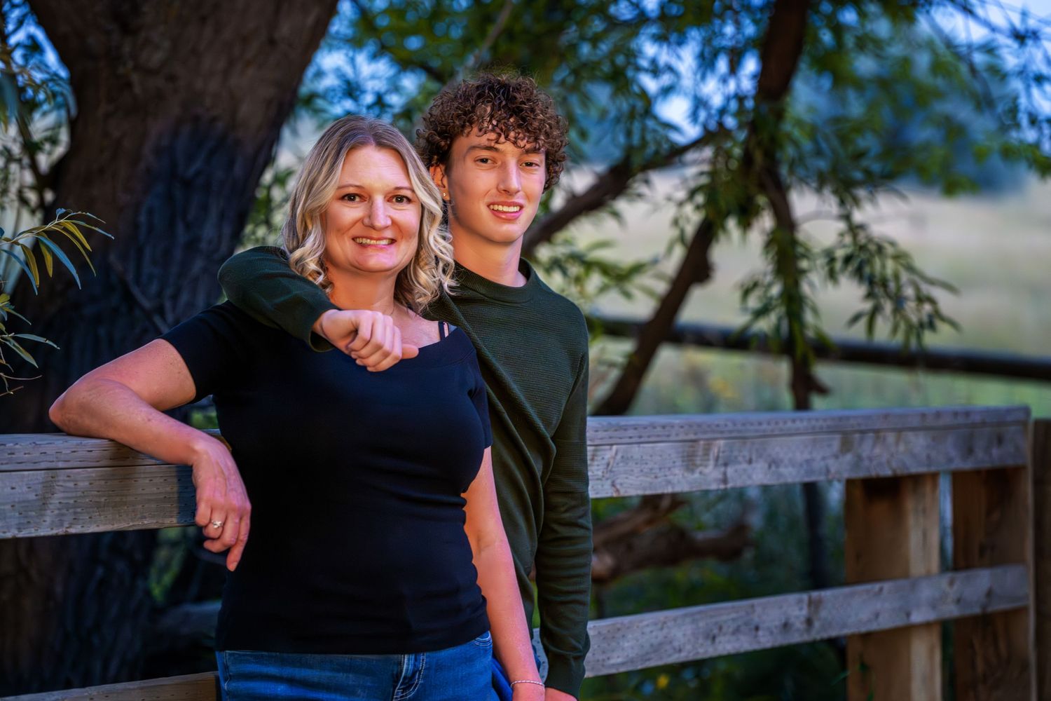 A Westminster Colorado Mother and Senior shares a tender moment together while sitting on a wooden fence at sunset.
