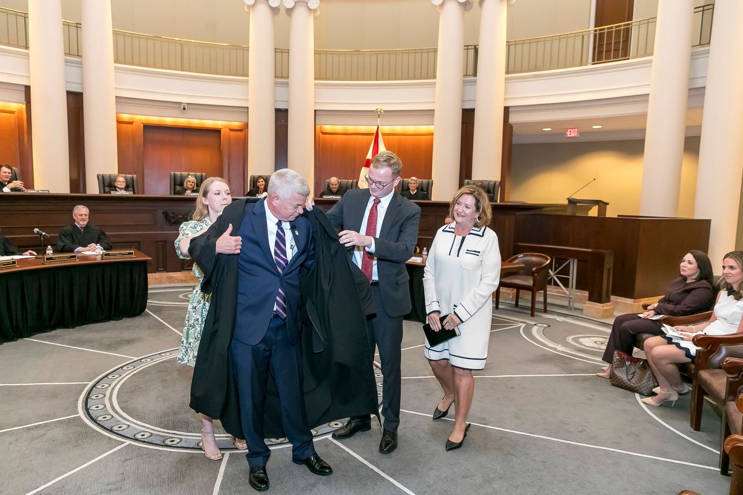 A group gathers in a grand circular rotunda with white columns and marble floors for a formal event.