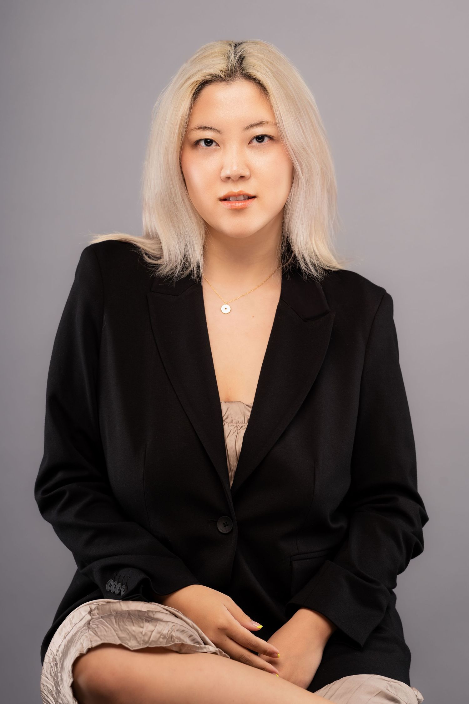 Professional studio portrait series showing a person with platinum blonde hair wearing a black blazer against a gray backdrop.