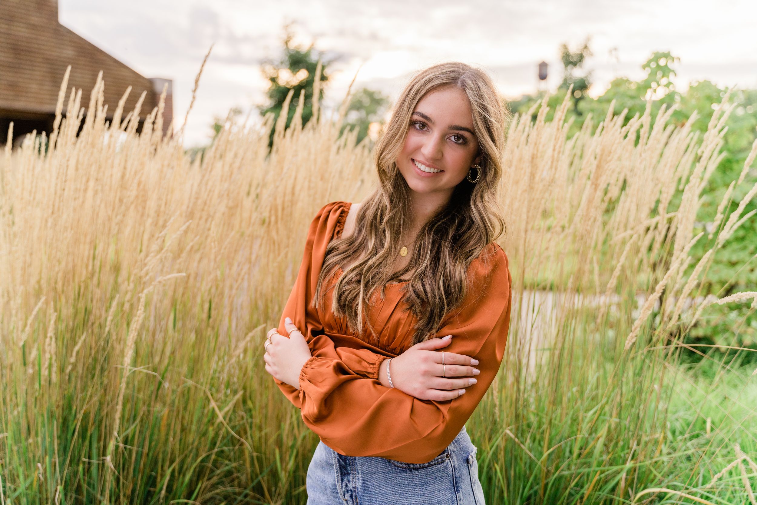 A person in an orange sweater poses in a field of tall grass during golden hour.