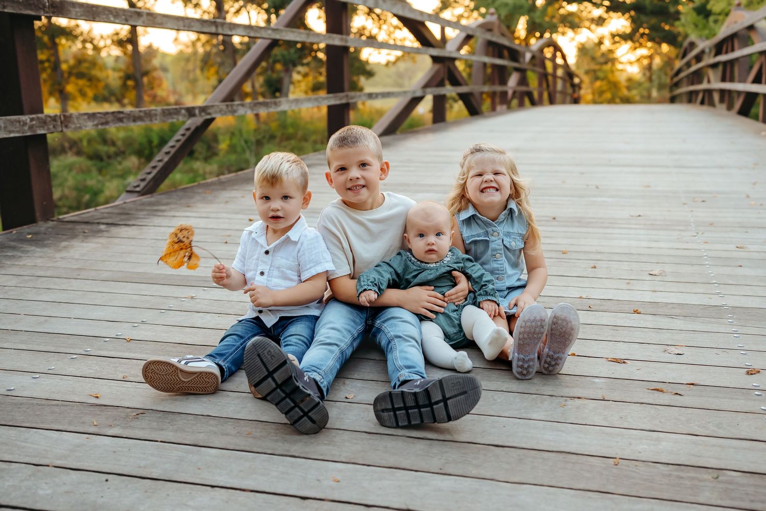Three children sit and laugh together on a wooden deck during a golden sunset photo session.