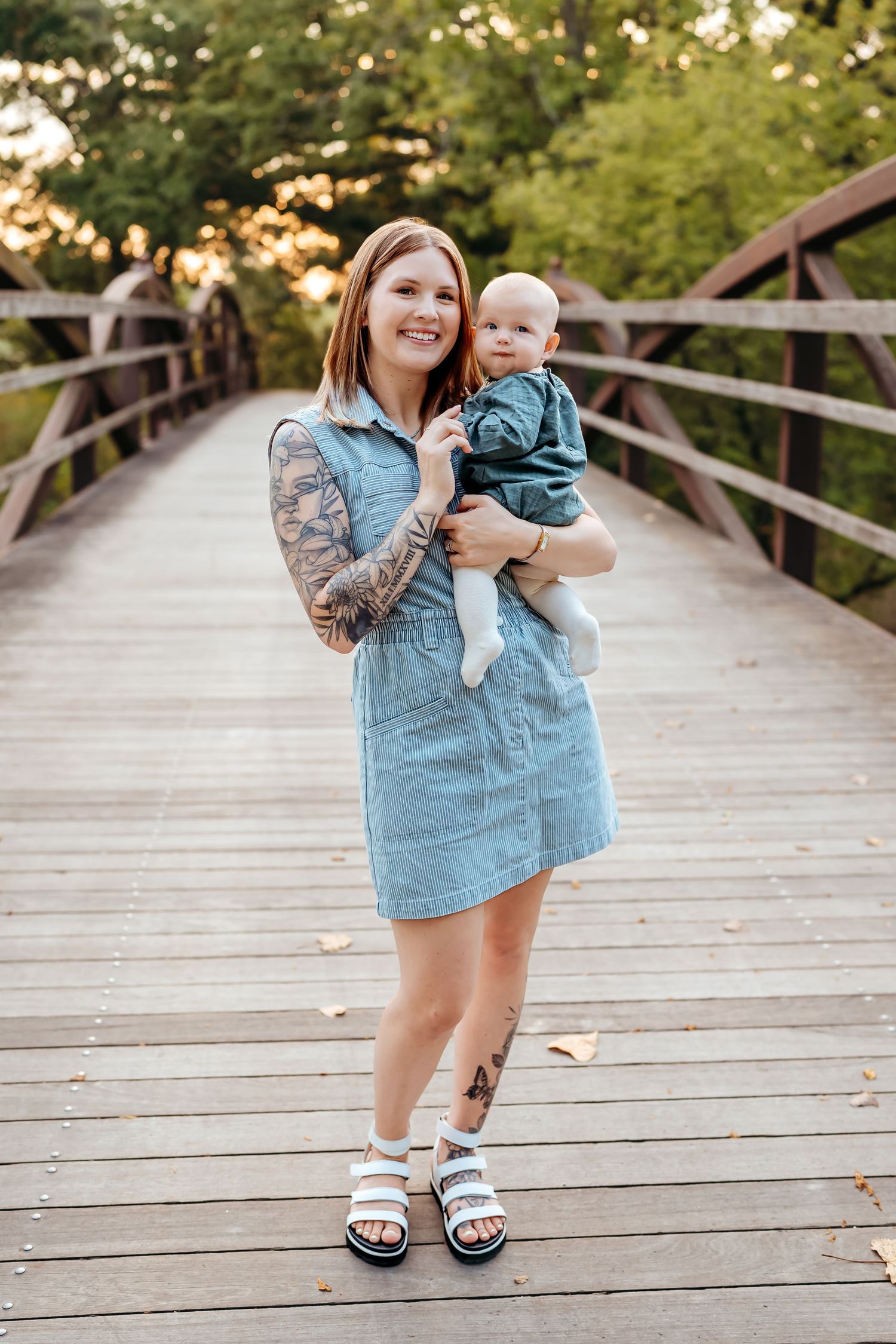 A parent and child stand together on a wooden bridge during sunset while wearing casual summer attire.