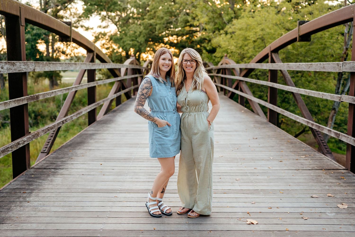 Couple walking hand in hand across a wooden bridge surrounded by lush green trees and nature.