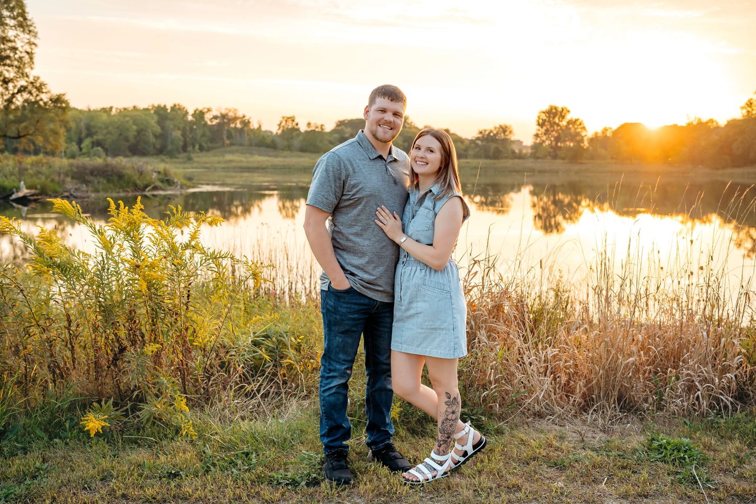 A romantic sunset photoshoot by a serene lake with tall grass and golden light creating a warm atmosphere.