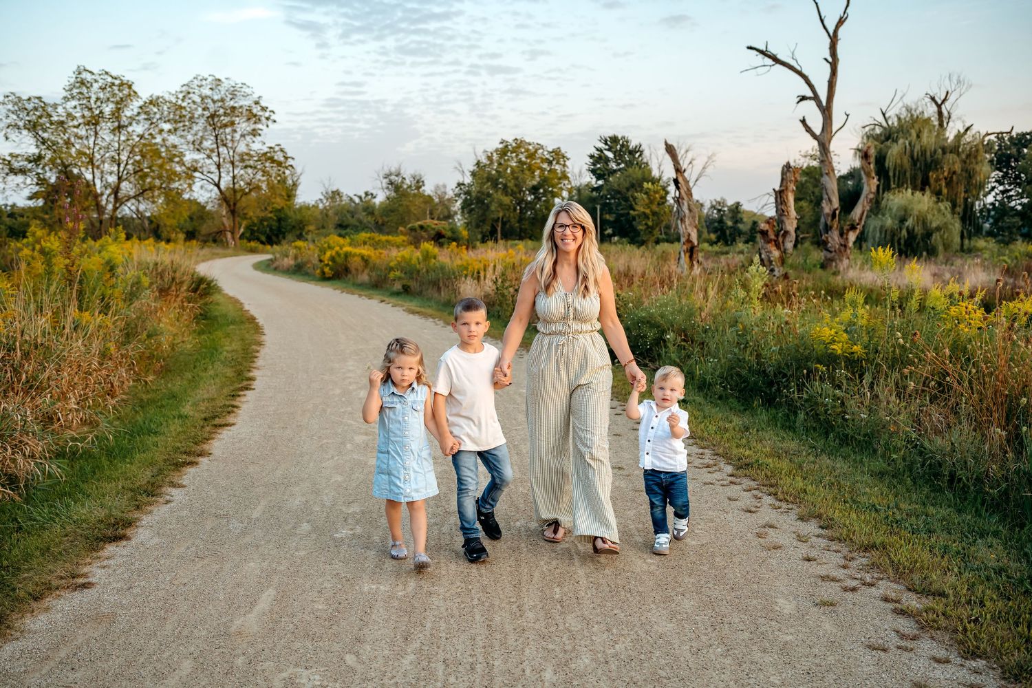 A group walks together on a winding gravel path through a natural landscape at sunset.