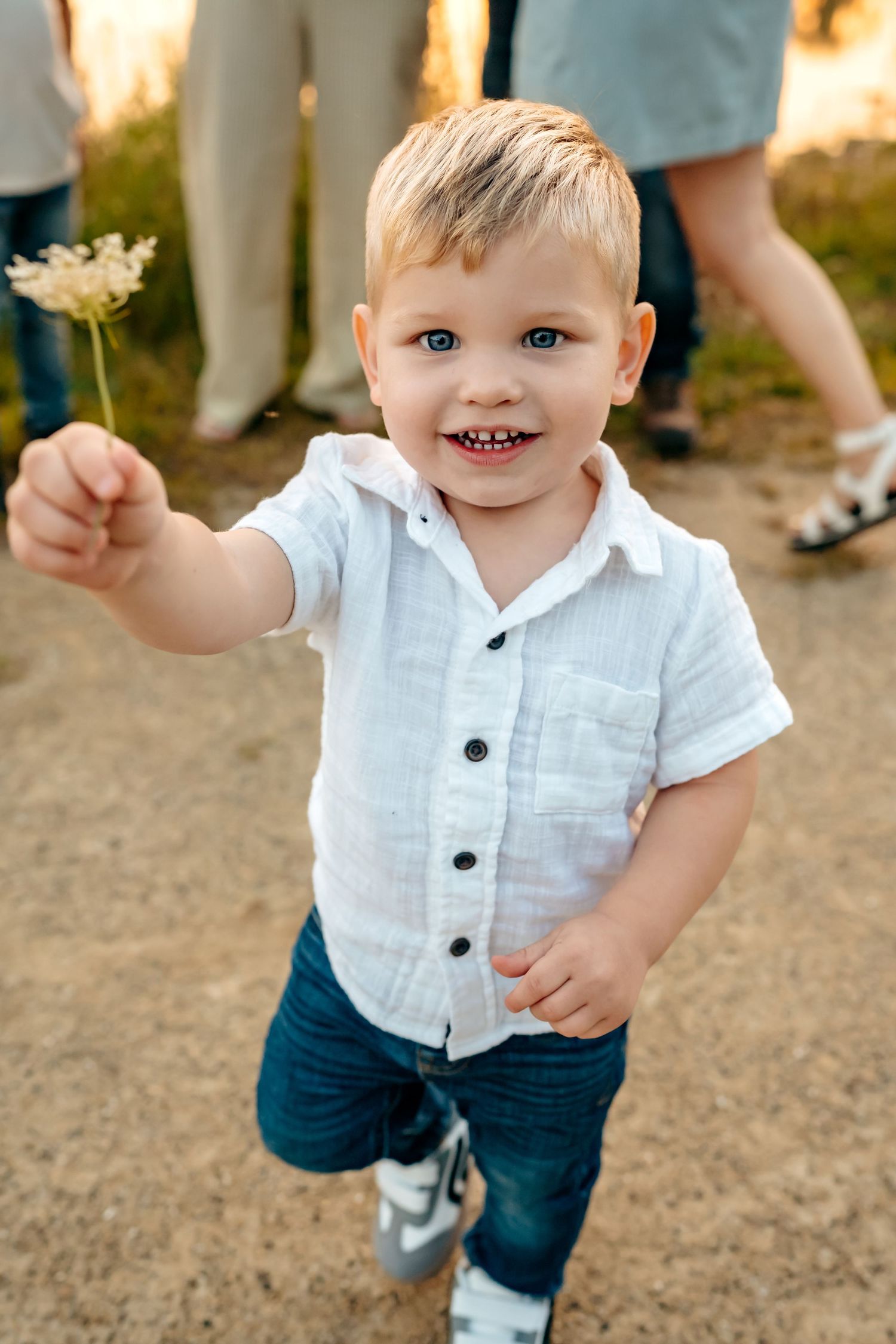 A child in a white button-down shirt and blue shorts smiles while playing outdoors.