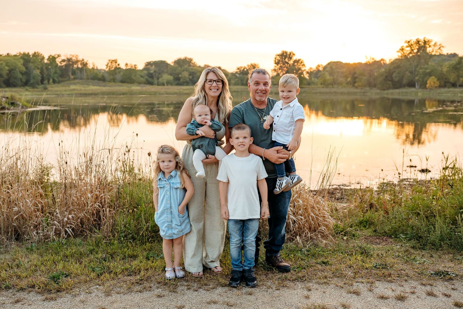 A group stands together at sunset by a lake with tall grass and golden light creating a warm autumn atmosphere.