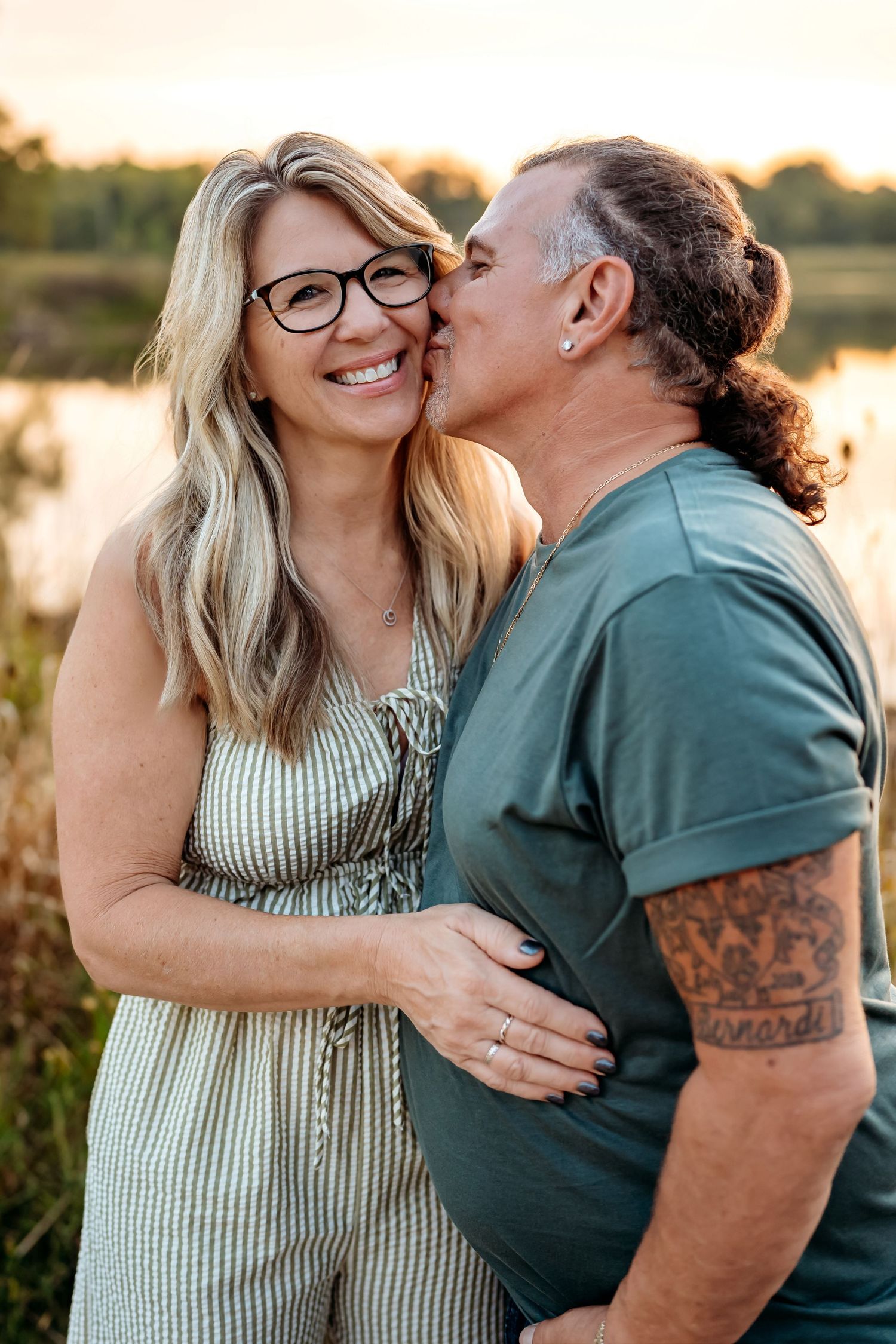 A romantic couple shares tender moments during a sunset photoshoot in a field wearing green and striped outfits.