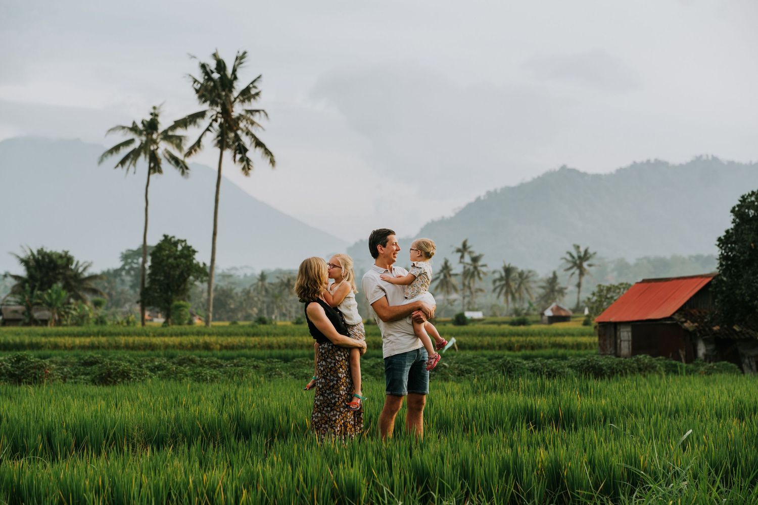 Family walking through lush green rice terraces with mountains in the background.
