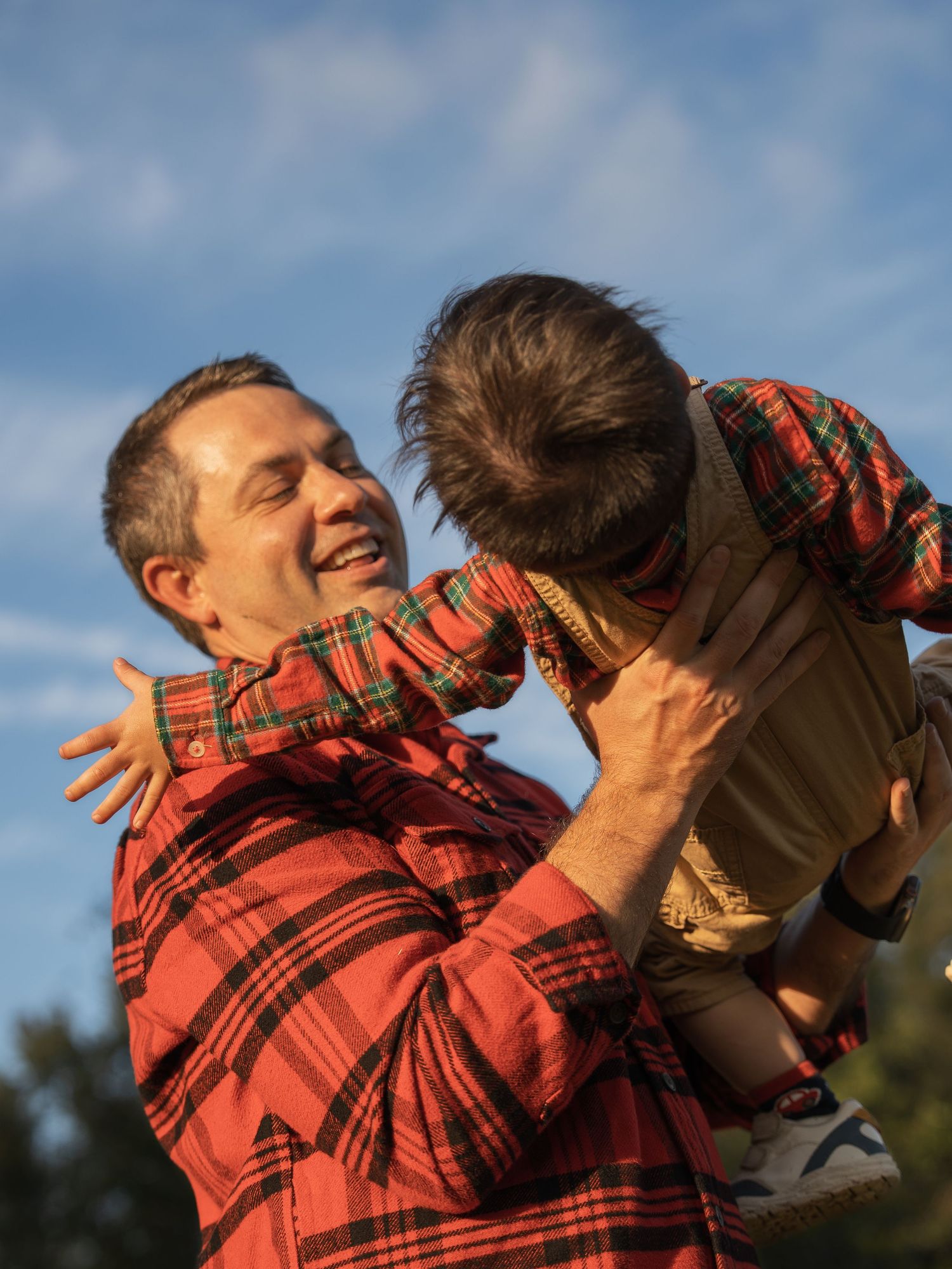 A joyful moment captured outdoors as an adult playfully lifts a small child against a blue sky background.