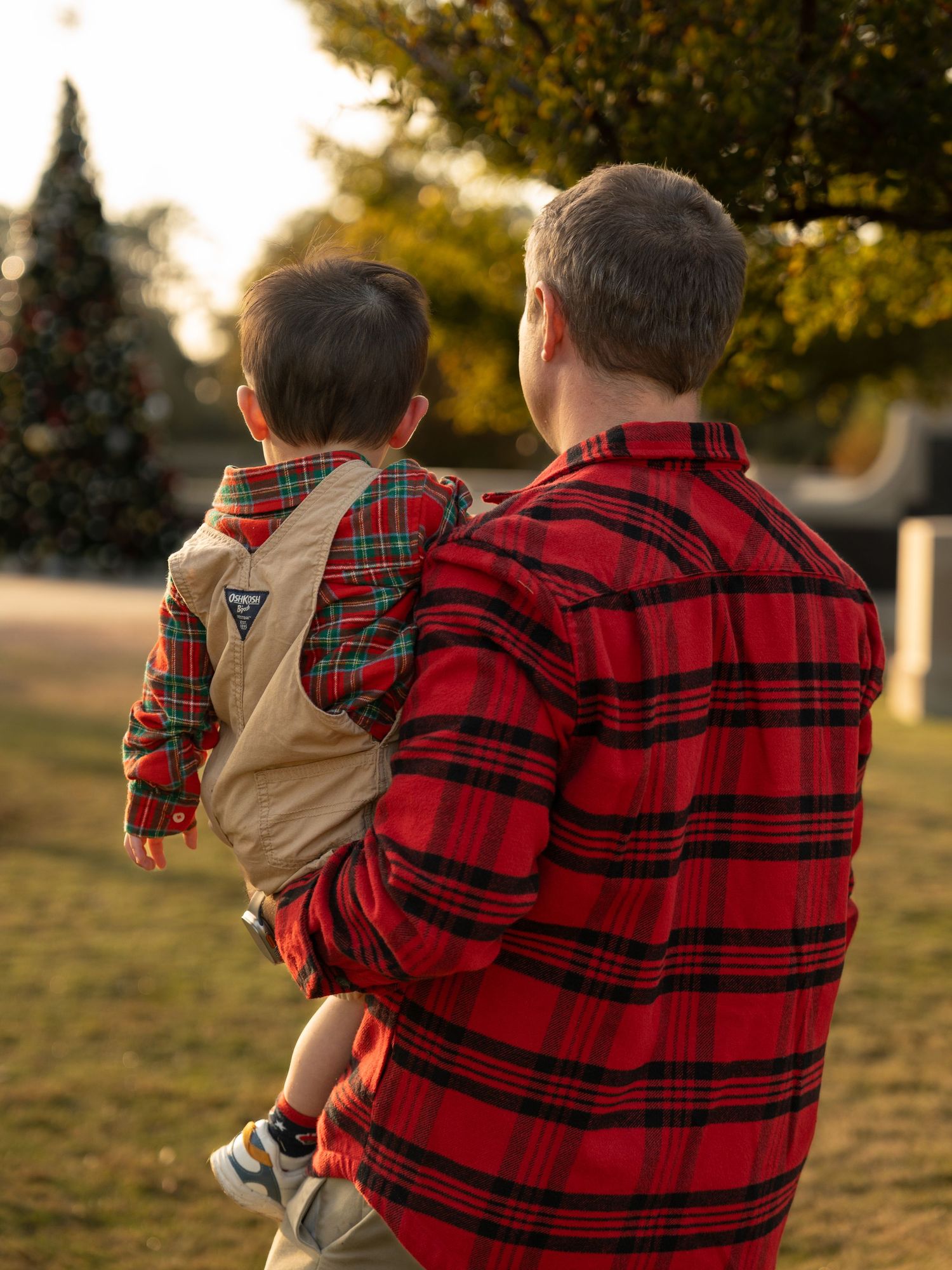 Parent and child in matching red buffalo plaid shirts walk together in a grassy field at sunset.