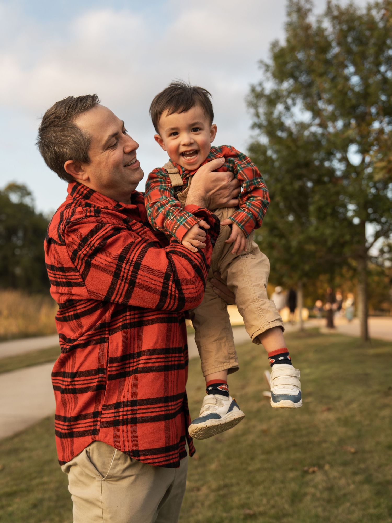 Parent and child wearing matching red plaid shirts share playful moments in a grassy outdoor setting.