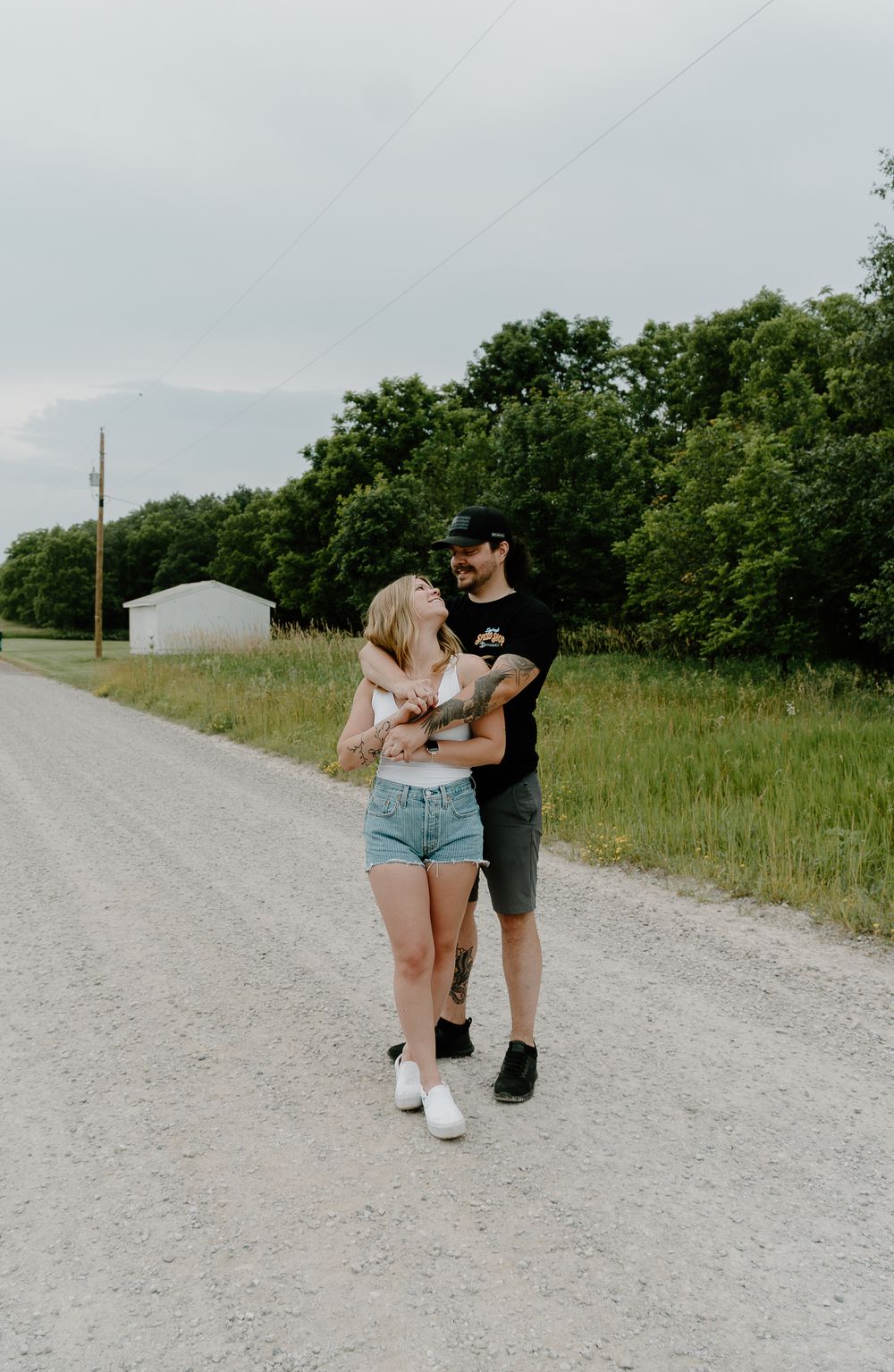 A couple walks together on a gravel path surrounded by green fields on a summer day.
