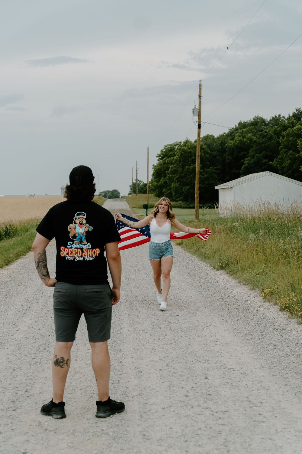 Two people walking on a gravel path carrying an American flag on a sunny day.