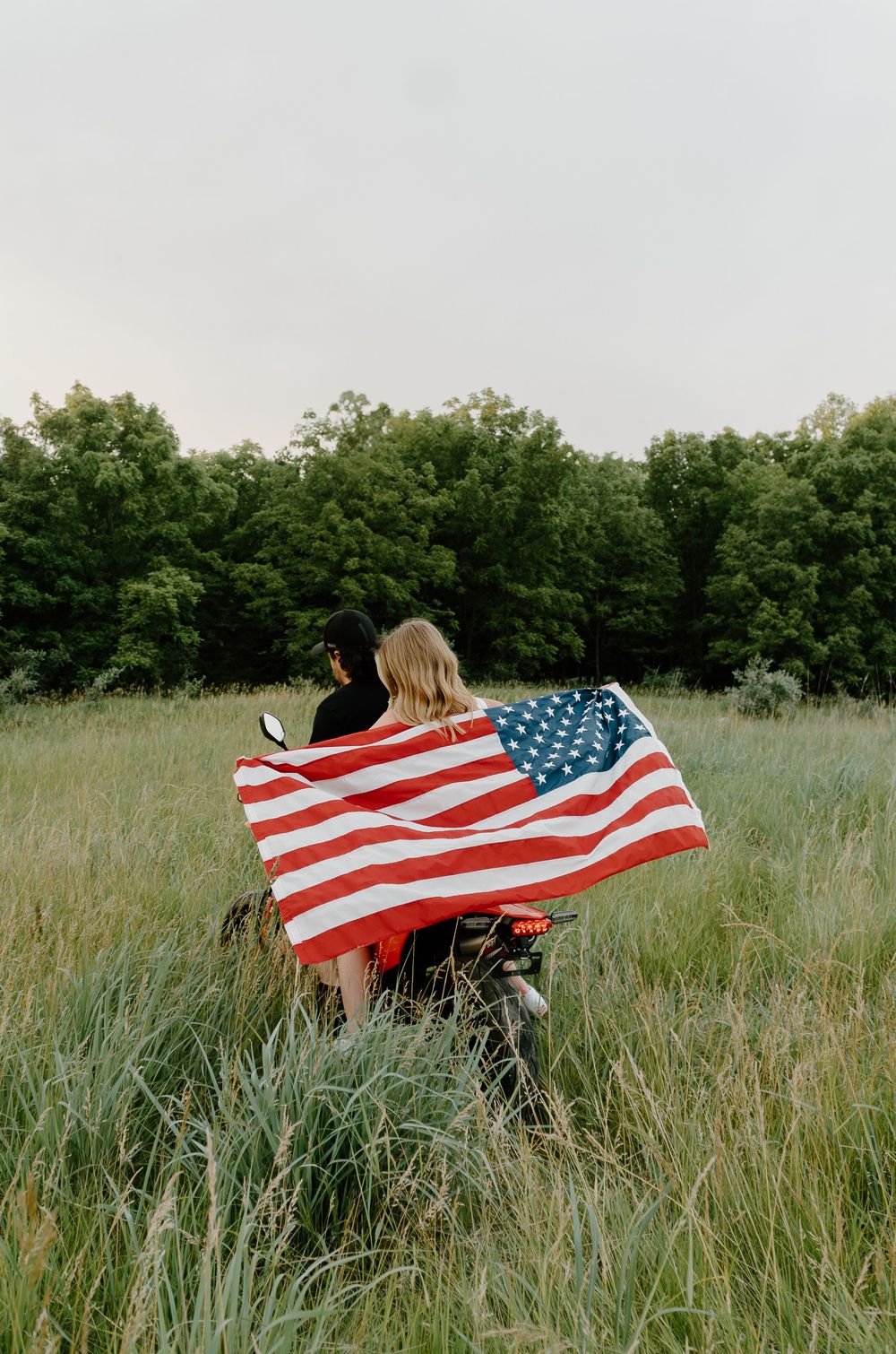 People holding an American flag in a grassy meadow with trees in the background during golden hour.
